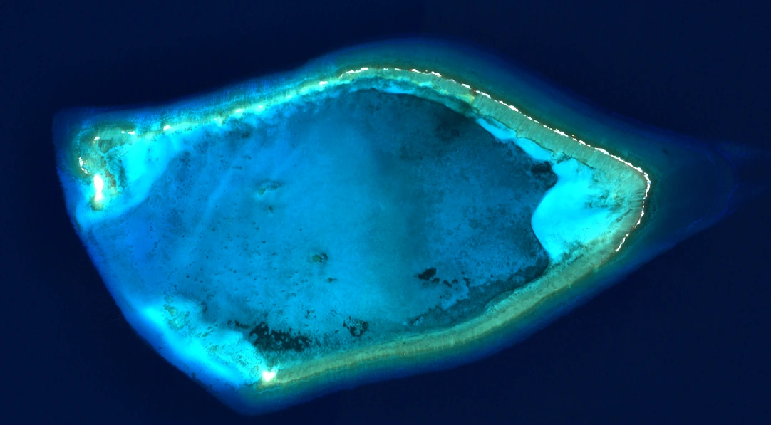 True-colour satellite capture of a clear atoll lagoon in the Bahamas, turquoise shallows inside a reef rim on dark open water.