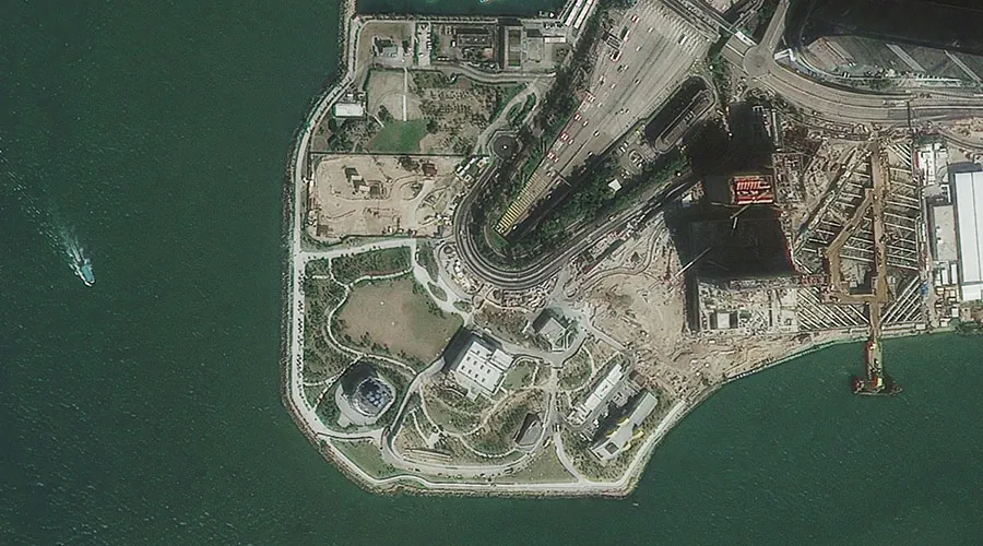 Port headland with reclaimed ground, bulk stockpiles and a wharf under construction, seen from above
