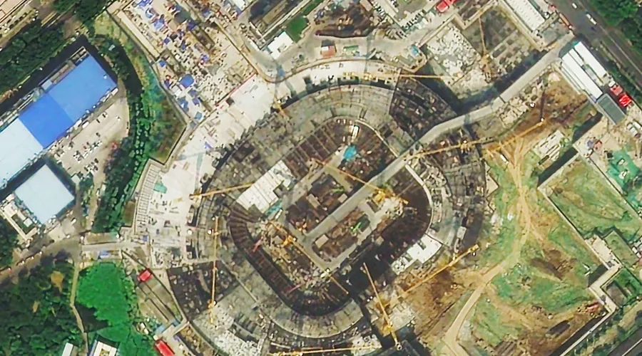 Stadium under construction, tower cranes ringing an excavated bowl, seen from directly above